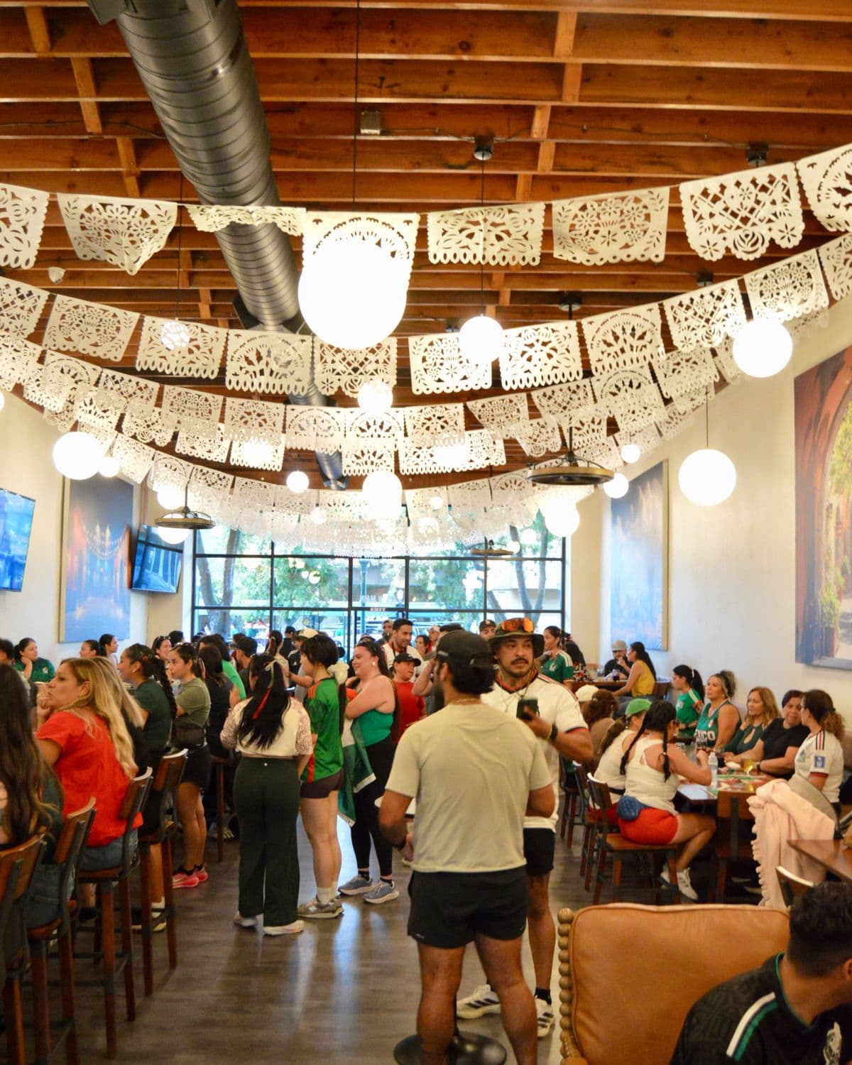 The taproom full of people under strings of papel picado.
